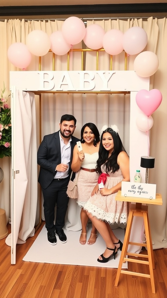 A charming photo booth at a baby shower with pink balloons and a sign that says 'BABY'. Three friends are posing happily in front of it.