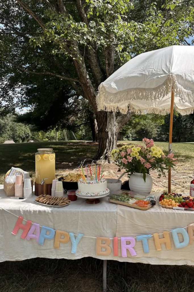 Outdoor birthday food and drink table with cake and fruit