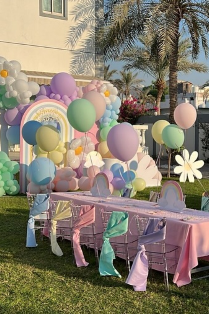 Pastel rainbow birthday table with balloons and clear chairs