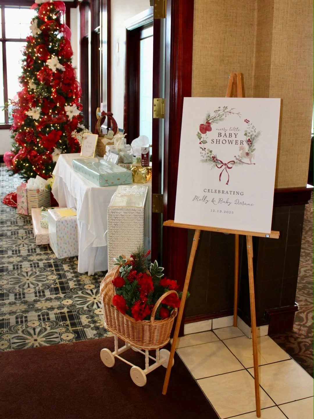 Santa Baby shower welcome easel with red flowers, gifts, and a decorated Christmas tree