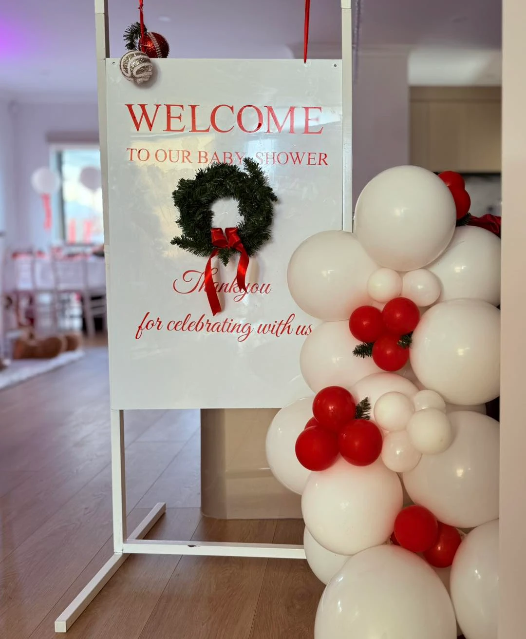 White Santa Baby welcome sign decorated with a green wreath and white and red balloons