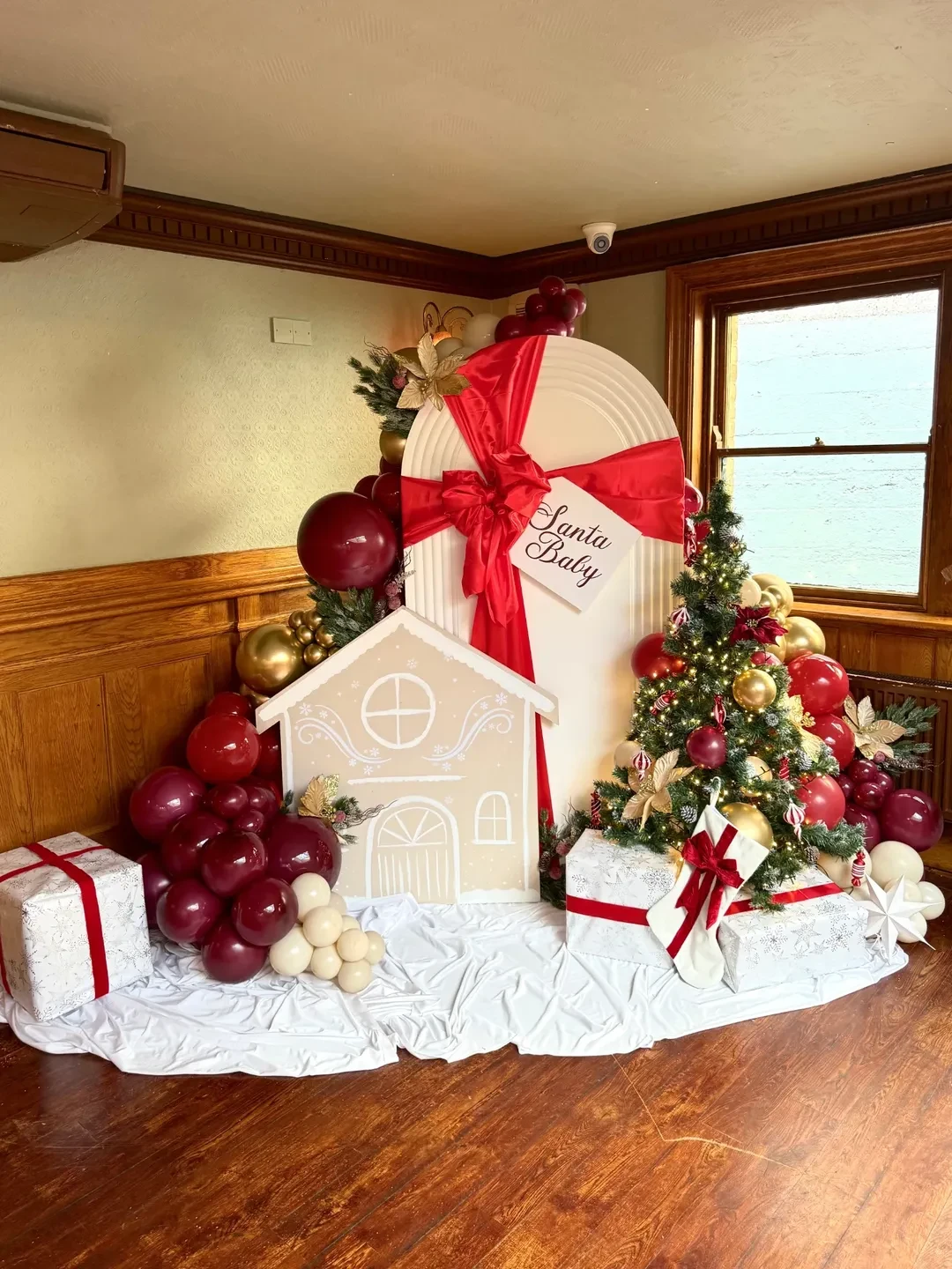 Gingerbread arch photo corner with burgundy balloons, gift boxes, and a miniature Christmas tree