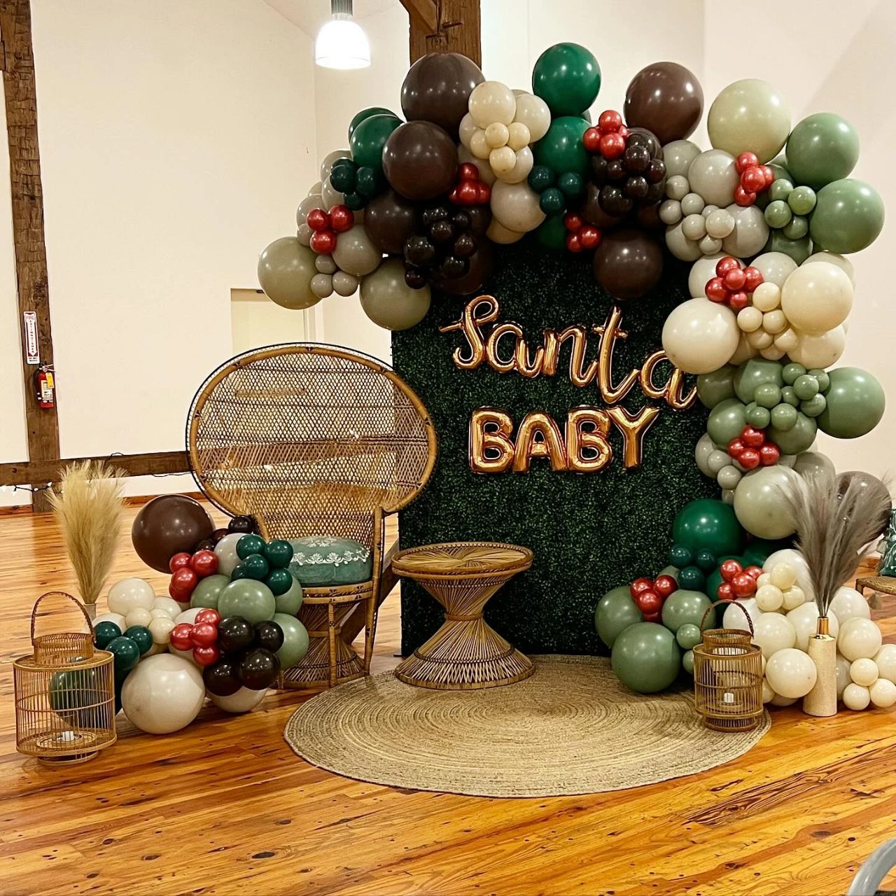 Boho Santa Baby backdrop with green and neutral balloons, a peacock chair, and pampas grass