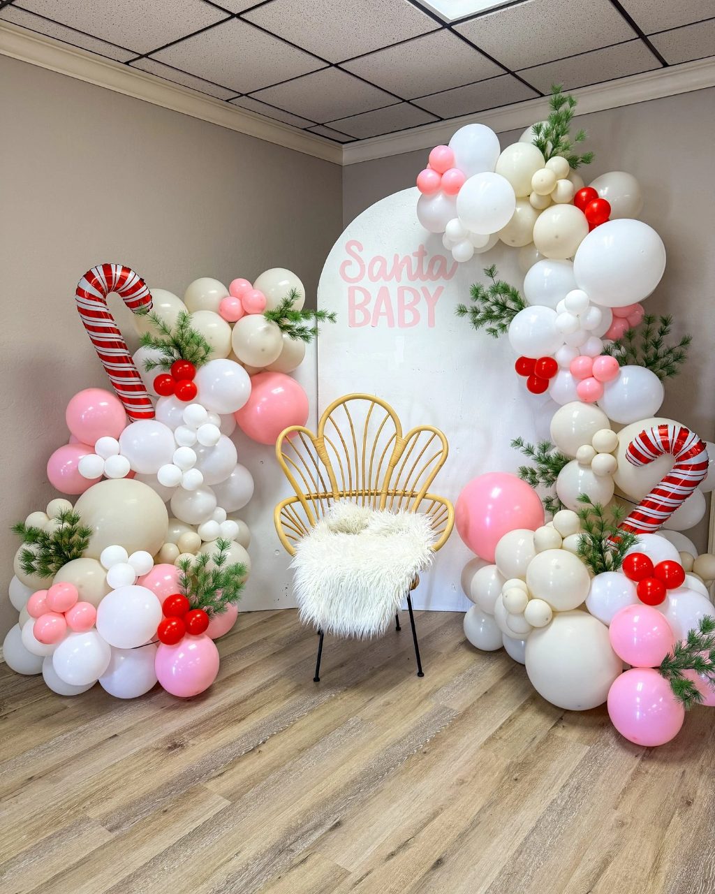 Pastel pink Santa Baby photo zone with balloons, candy cane decorations, and a bohemian chair
