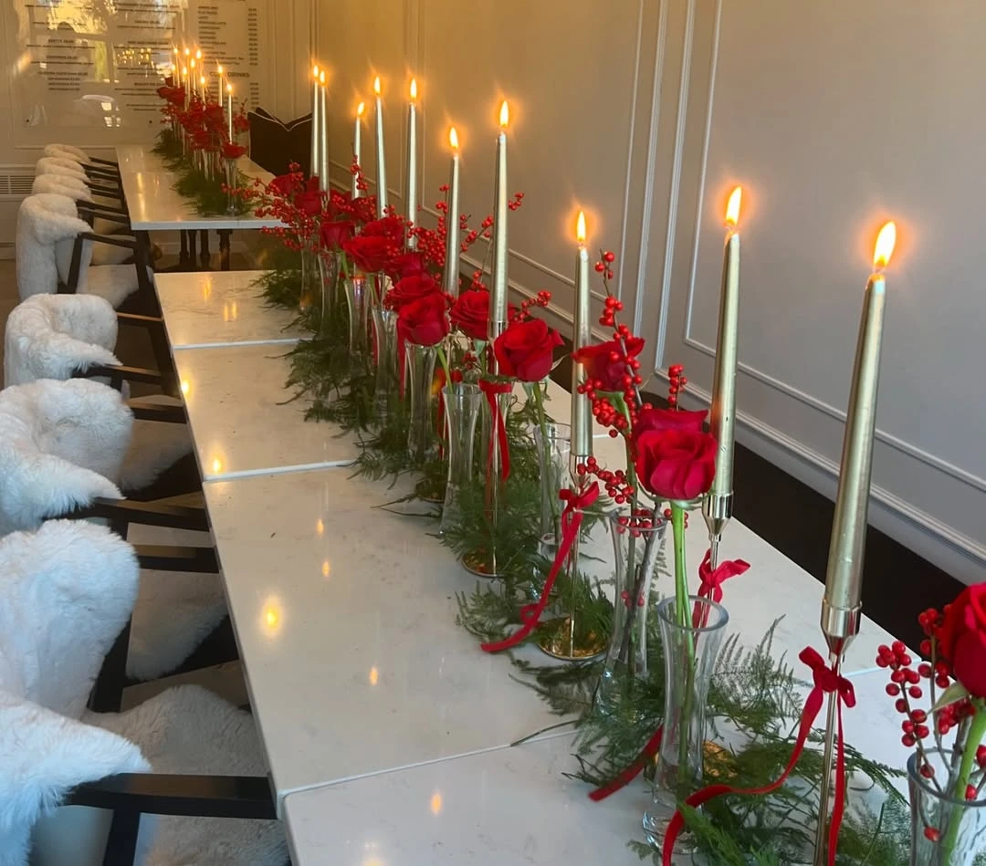 Candlelit baby shower table with red roses, pine greenery, berries, and gold taper candles
