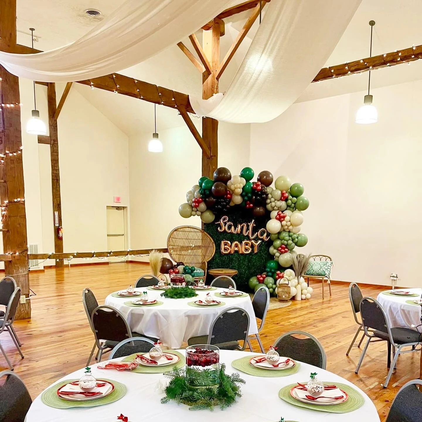 Spacious barn baby shower venue with balloon decor, round tables, greenery, and string lights