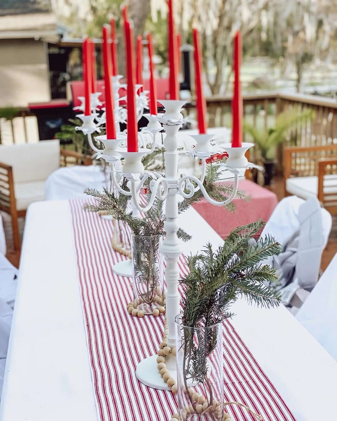 Outdoor Santa Baby table with white candelabras, red taper candles, pine branches, and striped table decor